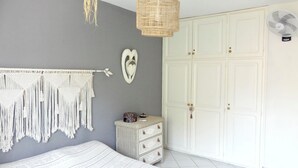 Ein Schlafzimmer mit grauer Wand, Wandbehängen aus Makramee, einer weißen Kommode und einem weißen Kleiderschrank.