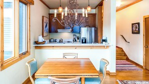 Een keuken met houten kastjes, een roestvrijstalen koelkast, een kroonluchter en een eettafel met stoelen.