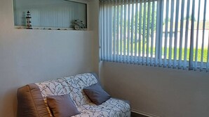 Ein modernes Wohnzimmer mit einem braunen Ledersofa, einem Couchtisch mit Glasplatte und einem großen Fenster mit vertikalen Jalousien.