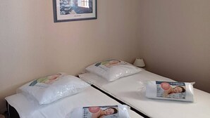 Ein Hotelzimmer mit zwei Einzelbetten, jeweils mit Kissen und Decke. Darüber an der Wand hängt ein gerahmtes Bild.