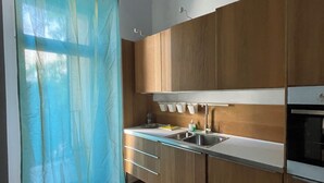 A modern kitchen with wooden cabinets, a stainless steel sink, and a window with a blue curtain. - apartment in Katowice center/ 2 min - train station (Katowice)