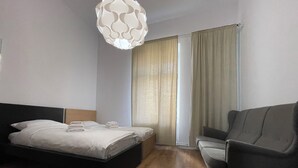 A hotel room with a bed, a chair, a window with curtains, and a hanging light fixture. - apartment in Katowice center/ 2 min - train station (Katowice)