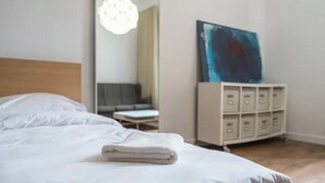 A neatly made bed with a folded white towel, a bedside table, a modern lamp, a painting on the wall, and a white storage unit. - apartment in Katowice center/ 2 min - train station (Katowice)