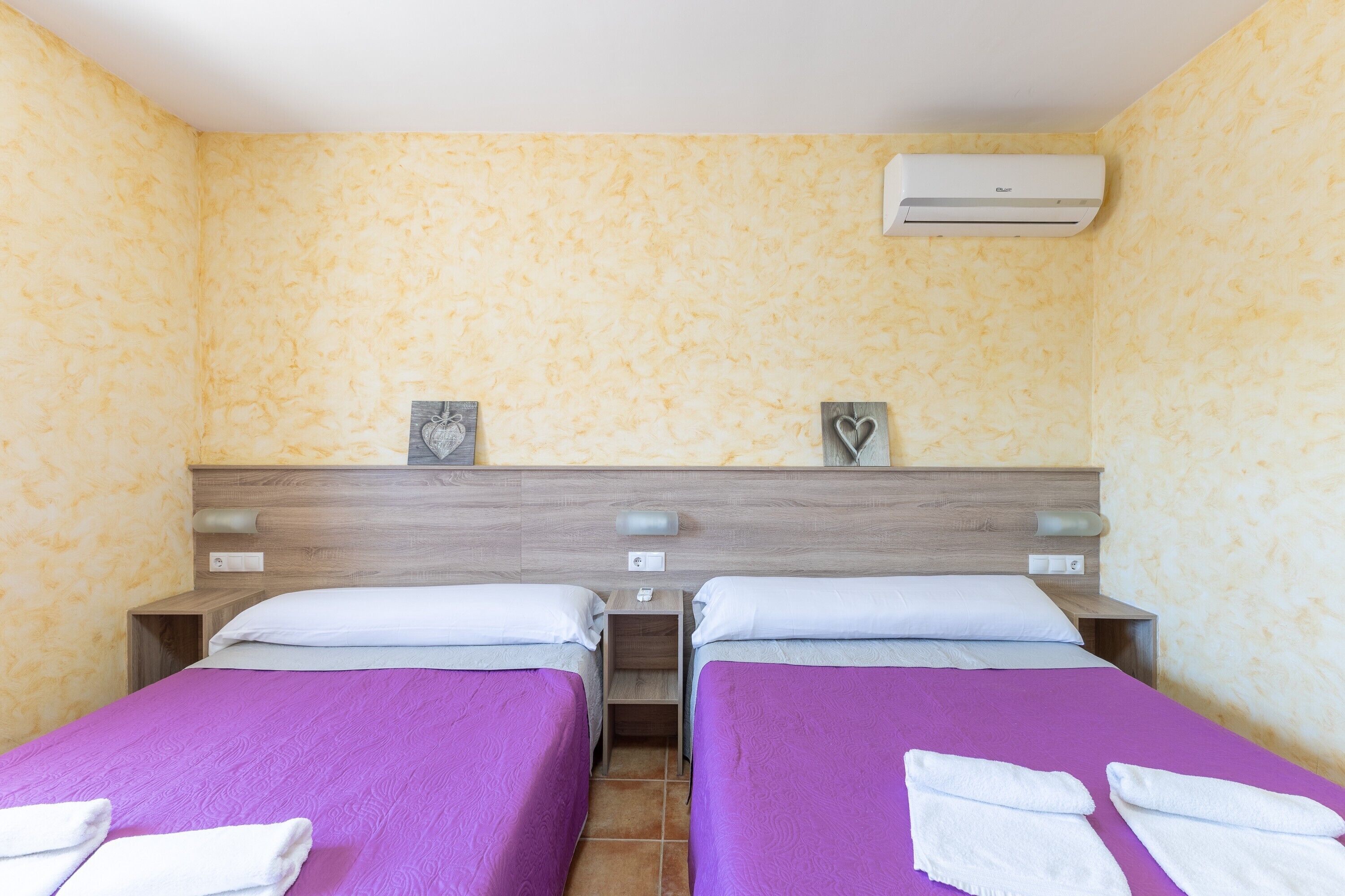 Una habitación de hotel con dos camas, cabeceros de madera y un equipo de aire acondicionado.