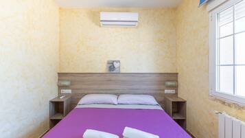 Una habitación de hotel con cama, mesita de noche, aire acondicionado instalado en la pared y ventana.