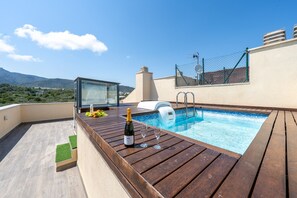 A rooftop pool with a wooden deck, a bottle of champagne, and two glasses.
