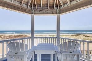 A wooden gazebo with a table and two Adirondack chairs overlooking a beach. - All Inn | Oceanfront | Private Pool and Hot Tub (Virginia Beach)