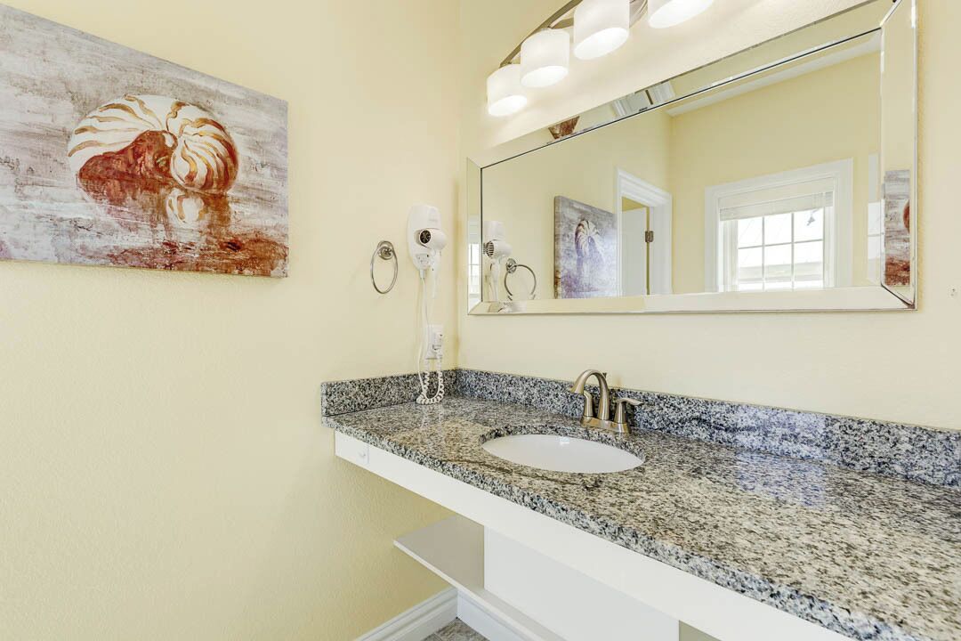 A bathroom with a granite countertop sink, a large mirror, and a wall-mounted hairdryer.