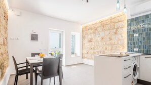 Una cocina moderna con una pared de acento de piedra, una zona de comedor con sillas de mimbre y una lavadora integrada.