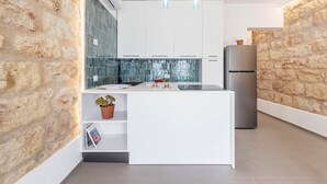 Una cocina moderna con una isla central, armarios blancos, un refrigerador de acero inoxidable y una pared de piedra.