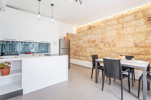 Una cocina moderna con pared de piedra, muebles blancos y una zona de comedor con mesa y sillas.