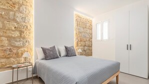 Un dormitorio con cama, mesita de noche, lámpara, armario y paredes de piedra.