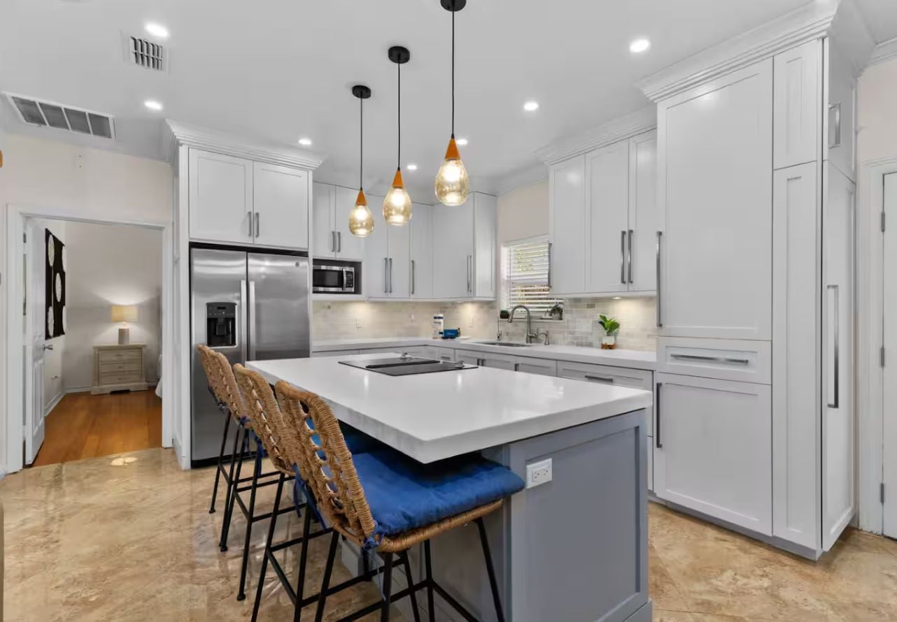A modern kitchen with white cabinetry, a central island with bar stools, and pendant lighting.