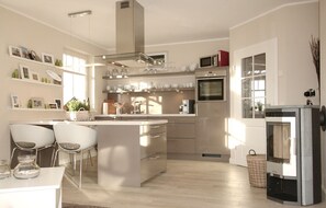 Une cuisine moderne dotée d’un îlot central, d’appareils électroménagers en acier inoxydable et d’un coin repas avec des chaises blanches.