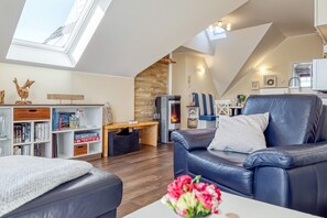 Un salón tipo loft con chimenea, un sofá de cuero, una estantería de madera y un tragaluz.