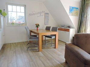 Ett modernt, väl upplyst rum med ett matbord, stolar, en soffa, en köksdel och ett fönster med utsikt över en balkong.