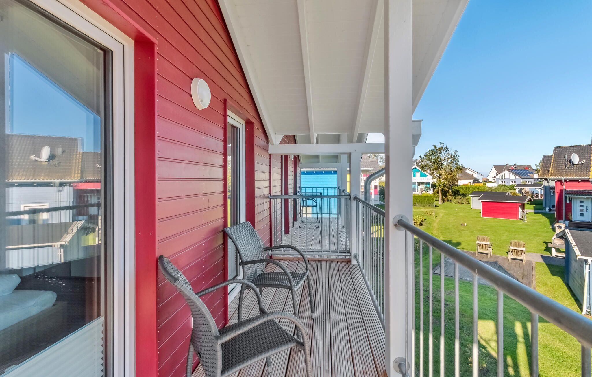A balcony with wicker chairs, a red exterior wall, and a view of a residential area.