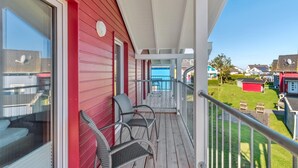 A balcony with wicker chairs, a red exterior wall, and a view of a residential area. - Lovely home in Süssau/Ostsee with sauna (Süssau/Ostsee)