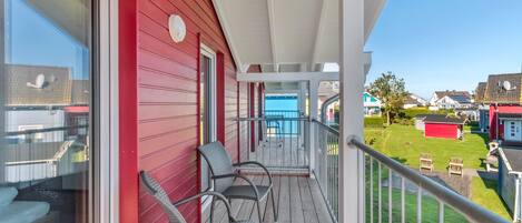 A balcony with wicker chairs, a red exterior wall, and a view of a residential area.