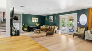 Amplia sala de estar con piso de madera, un sofá de cuero marrón, un sillón gris y una mesa de centro.