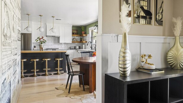 Una cocina moderna con armarios blancos, una isla de madera y taburetes negros. Hay un comedor con mesa y sillas de madera.
