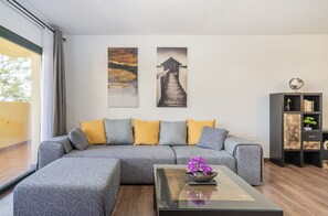 Un salon moderne avec un canapé d’angle, une table basse en verre et deux œuvres d’art accrochées au mur.