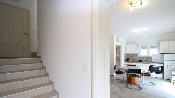 A modern kitchen with white cabinets, a dining area with a table and chairs, and a staircase leading to another level. - Apartment 2341/115071 (Istria - Fažana), 500m from the beach (Fažana)