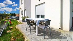 A patio with a table and chairs, a car parked in the background, and a building with a white exterior and a garage door. - Apartment 2341/115071 (Istria - Fažana), 500m from the beach (Fažana)