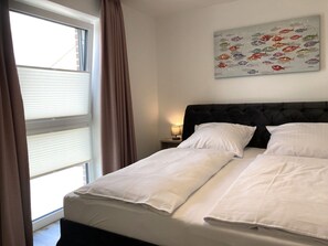 Un lit bien fait, avec du linge de lit blanc, une tête de lit sombre et un tableau représentant des poissons accroché au mur.