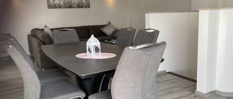 A modern dining area with a rectangular table, six grey upholstered chairs, a white decorative lantern, and a chandelier.