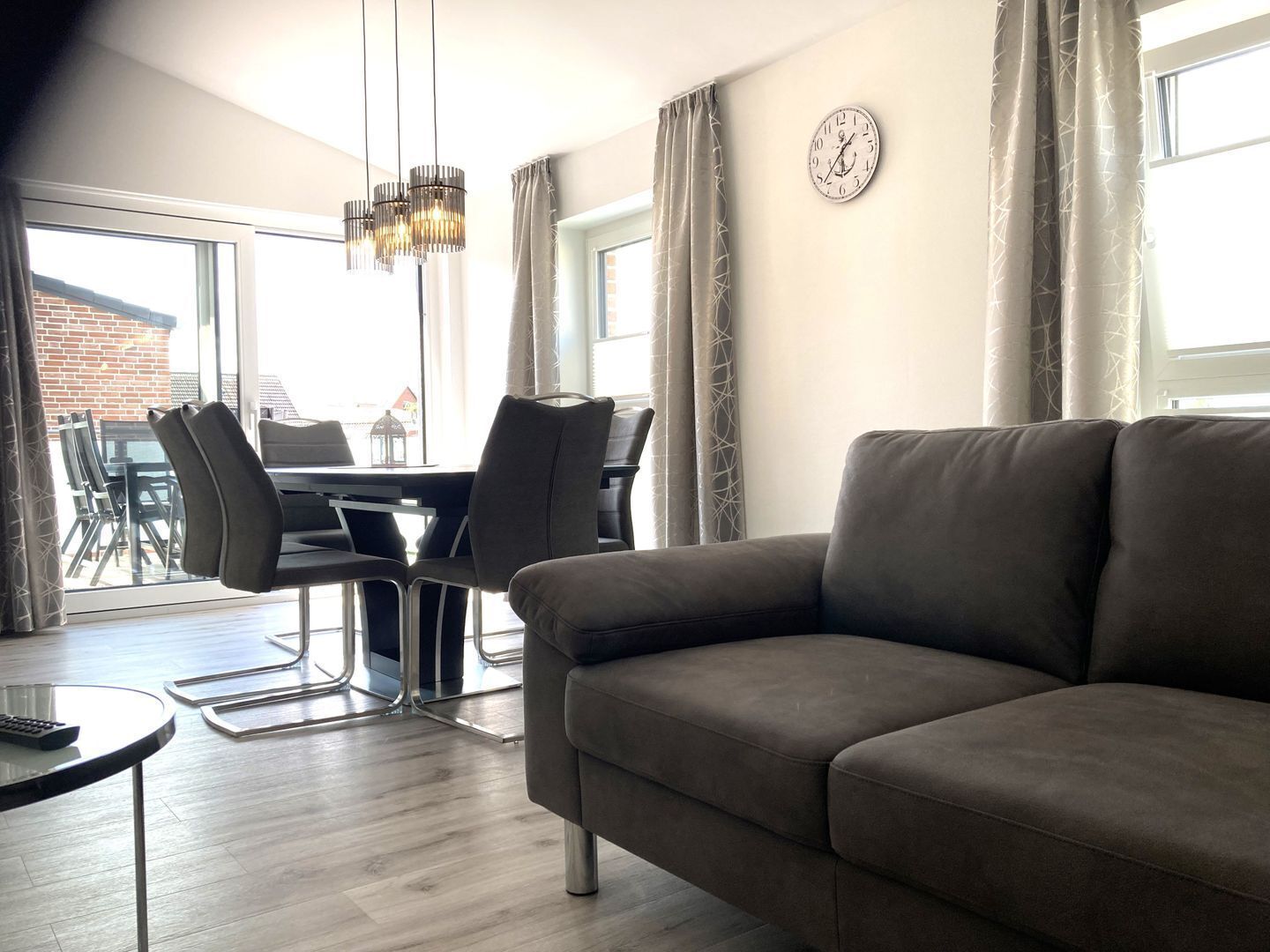 A modern living room with a sofa, dining table, chairs, and a chandelier.