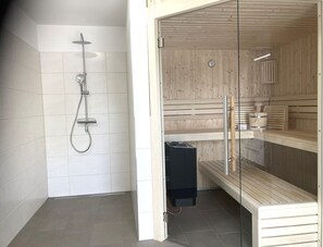 Une salle de bain moderne équipée d’une douche, d’un sauna et d’un banc en verre.