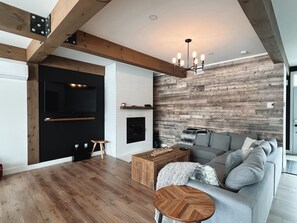 Ein modernes Wohnzimmer mit Holzboden, grauem Sofa, Couchtisch aus Holz und Kamin.
