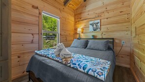 Quarto de cabana de madeira com cama, almofadas, abajur e um quadro na parede.