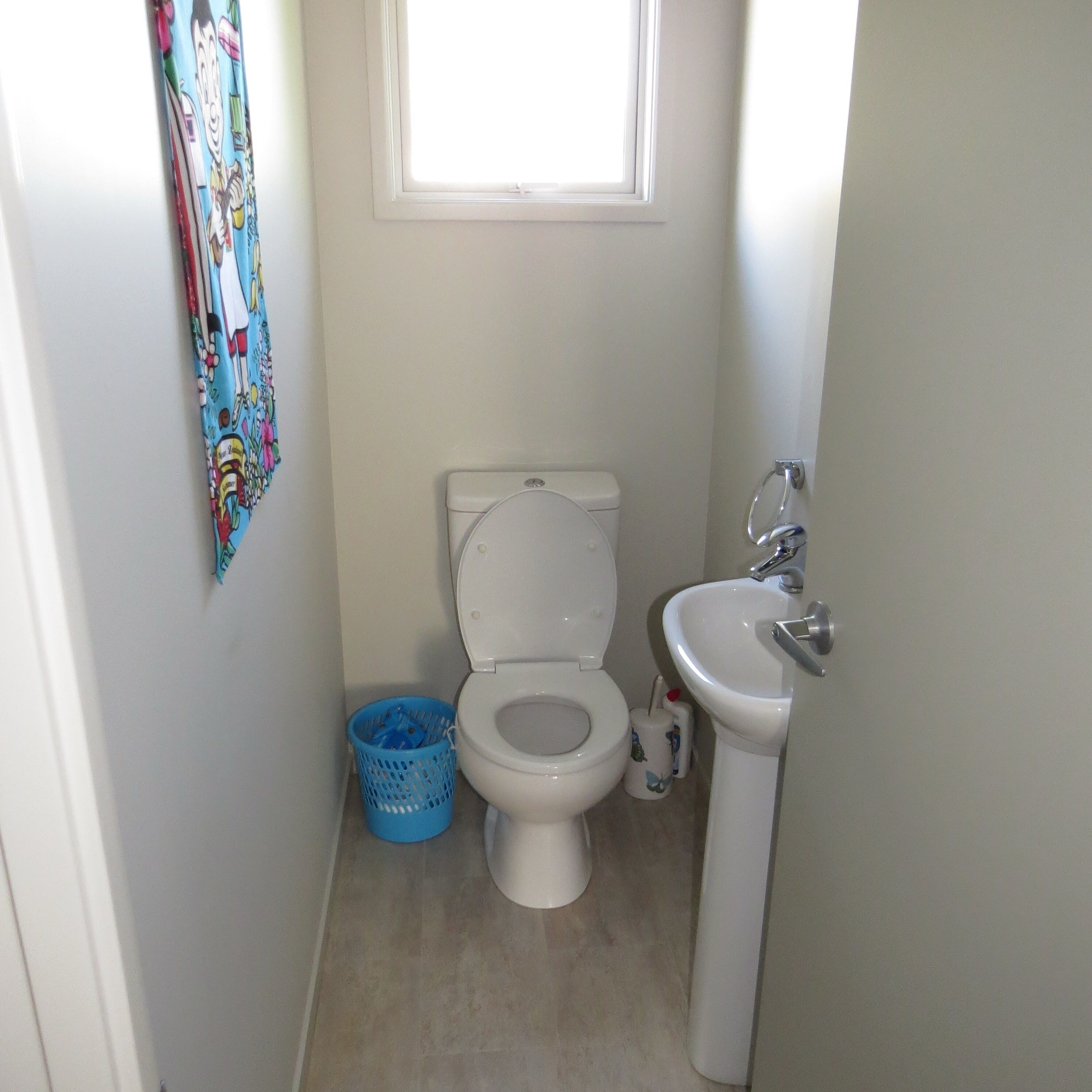 Une petite salle de bain propre, équipée de toilettes, d’un lavabo et d’une fenêtre située au-dessus des toilettes.
