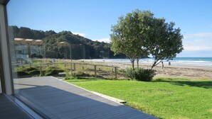 Vista desde una ventana sobre una playa con un muelle de madera, césped y un árbol.