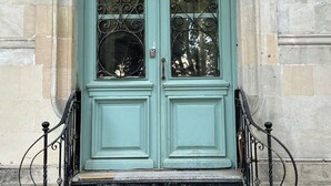 En turkis dør i dobbeltmodel med detaljeret jernbeslag, en lille postkasse og en bygningsfacade i sten.