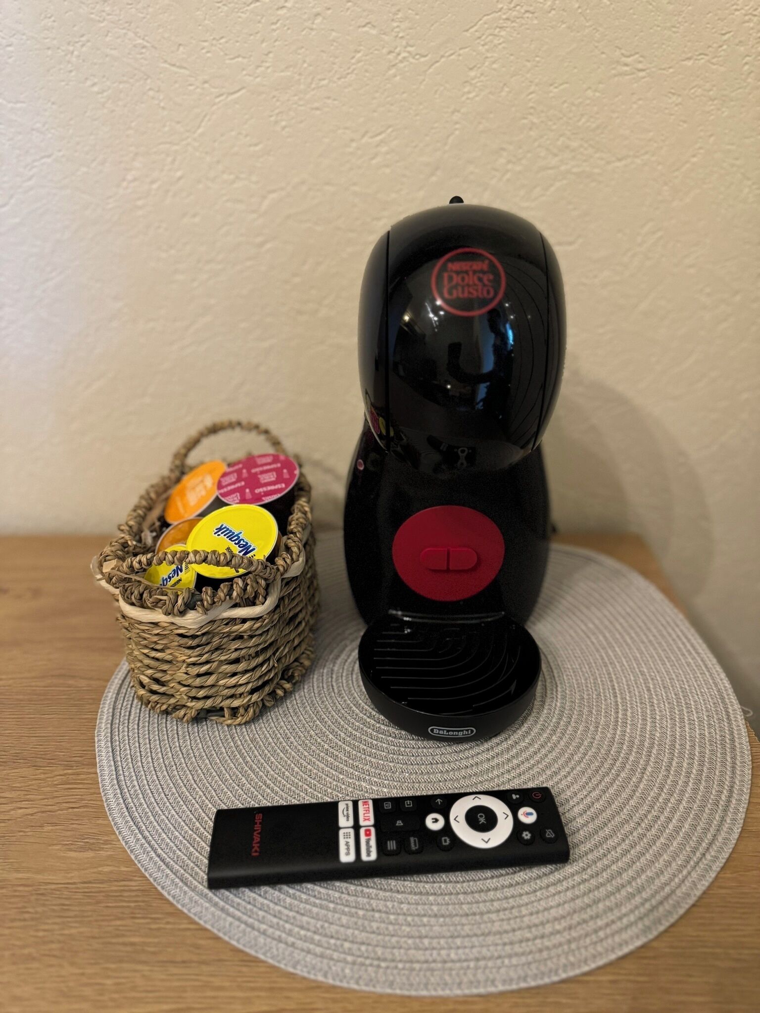 Un altavoz portátil negro con un botón rojo, un control remoto y una cesta de mimbre con aperitivos.