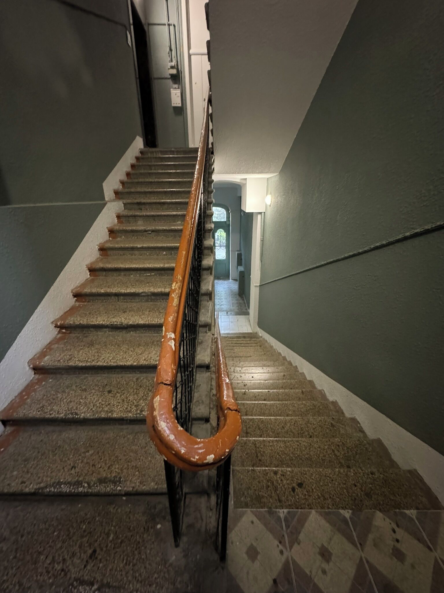 A staircase with a handrail, carpeted steps, and a tiled floor.