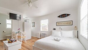 A white bedroom with a bed, a desk, a chair, a ceiling fan, and a window with blinds. - West Palm Beach Escape (West Palm Beach)