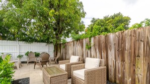 A patio area with wicker furniture, including two chairs and a small table, surrounded by a wooden fence and a white fence. - West Palm Beach Escape (West Palm Beach)