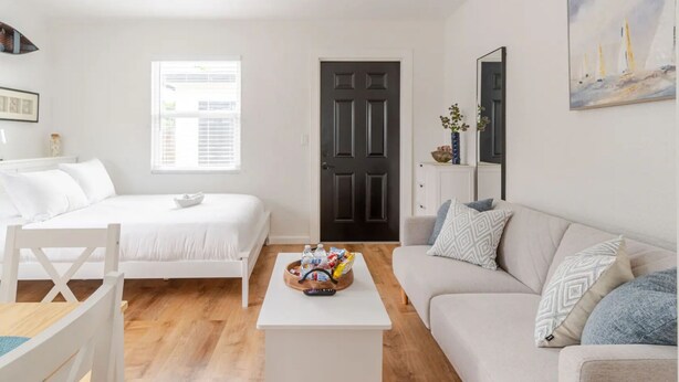A modern, well-lit living room with a bed, a sofa, a coffee table with snacks, and a door leading to another room. - West Palm Beach Escape (West Palm Beach)
