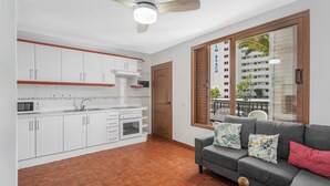 A compact kitchen with white cabinets and a red countertop, a gray sofa with patterned cushions, and a wooden door. - Vacation Apartment 'Apto Veracruz' with Shared Pool, Private Terrace and Wi-Fi (Costa Adeje)