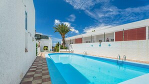 A swimming pool with a tiled deck, a palm tree, and a white building with red shutters. - Vacation Apartment 'Apto Veracruz' with Shared Pool, Private Terrace and Wi-Fi (Costa Adeje)