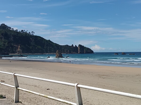 A beach with a metal railing, waves, and rocky cliffs.