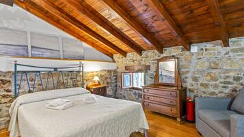 Un dormitorio con techo de madera, paredes de piedra, una cama, un aparador, un espejo y un extintor.