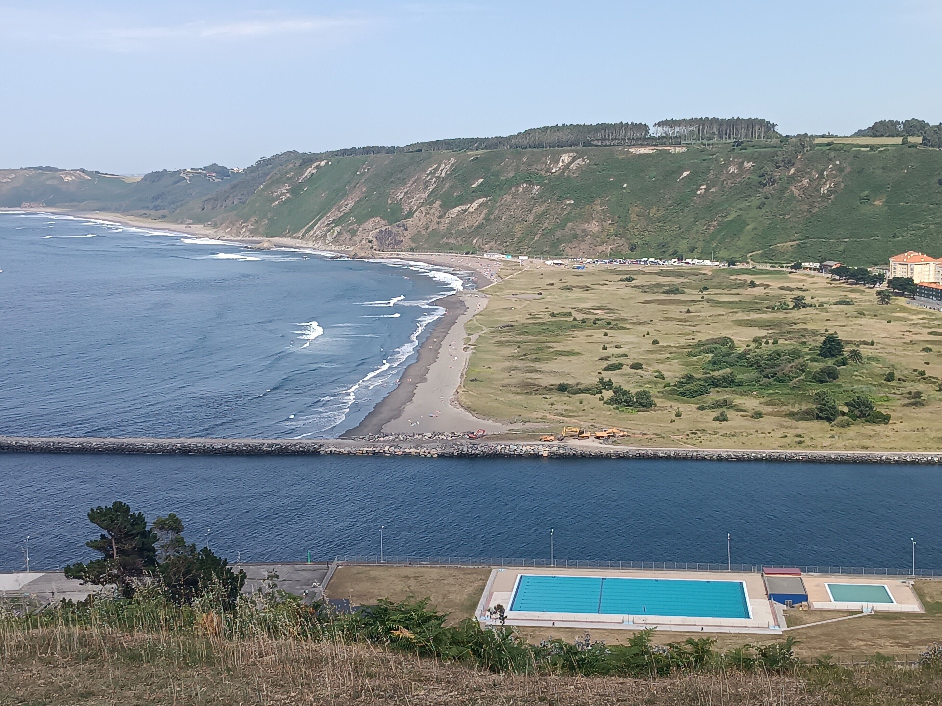 Un paisaje costero con piscina, playa y un telón de fondo montañoso.