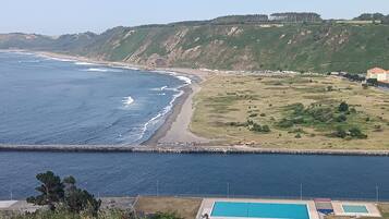 Un paisaje costero con piscina, playa y un telón de fondo montañoso.