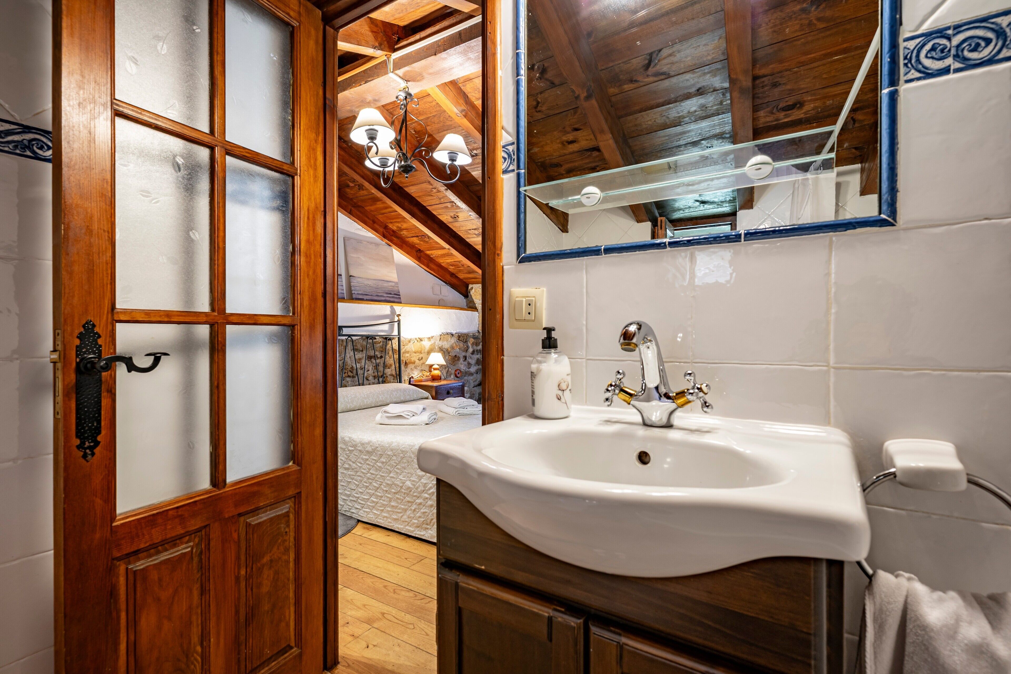 Un baño con puerta de madera, lavamanos blanco y espejo con marco azul.