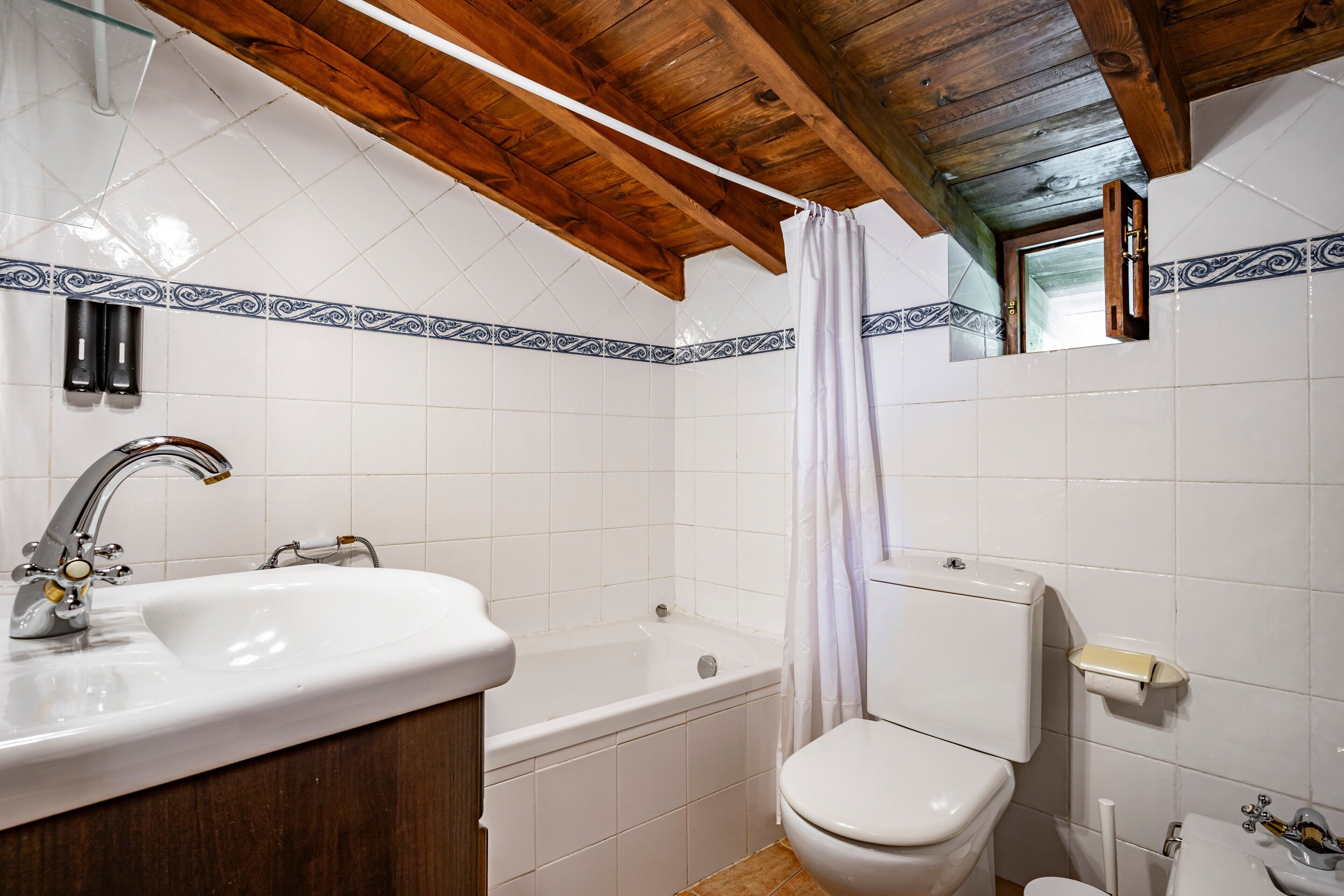 A bathroom with a sink, bathtub, toilet, and wooden ceiling beams.